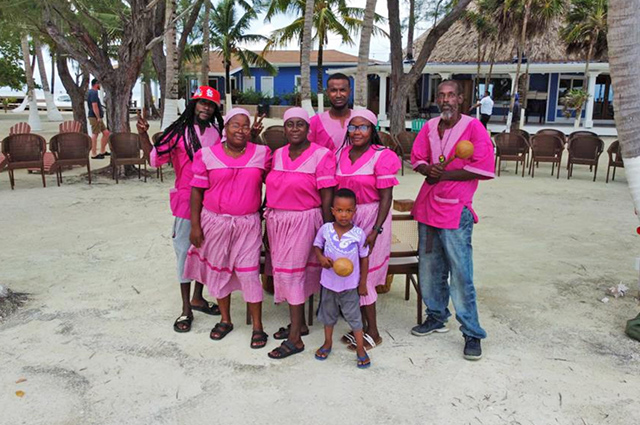 A smiling group of Garifuna drummers and dancers in pink attire at Coco Plum Island Resort.