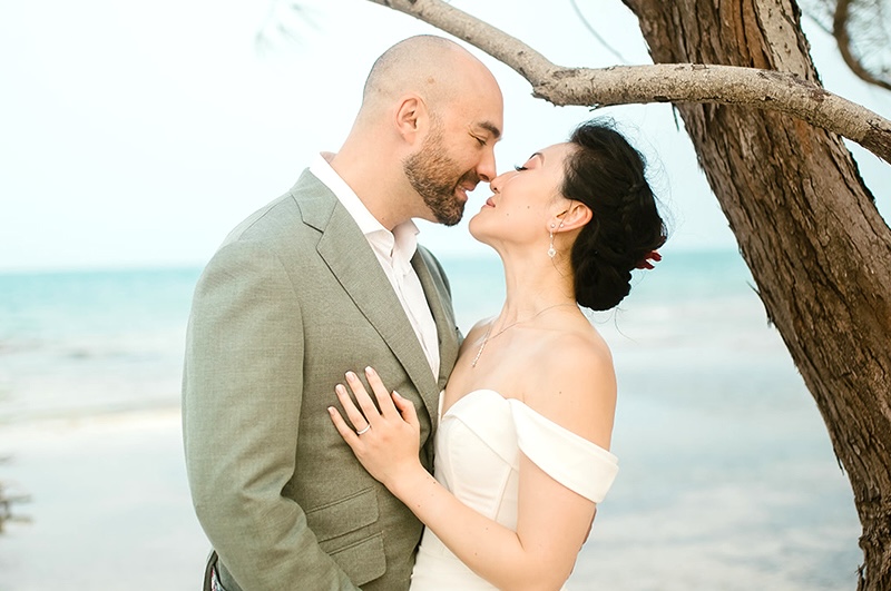 Bride and groom share a romantic moment under a tree on a private island, just before their wedding