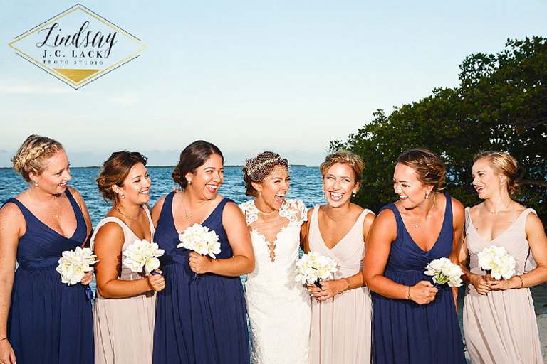 Bride laughing with her bridesmaids posing by the sea during a tropical destination wedding.