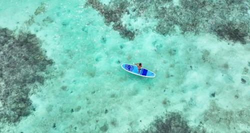Aerial view of turquoise ocean with a person paddleboarding.