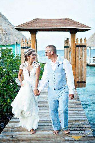 Bride and groom walk hand-in-hand barefoot on a wooden dock.