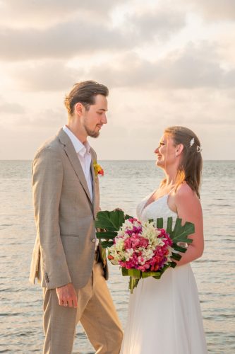 Bride and groom standing by the sea at golden hour.
